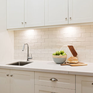 Large traditional kitchen pantry ideas - Large elegant galley kitchen pantry photo in Hobart with a farmhouse sink, shaker cabinets, white cabinets, granite countertops, white backsplash, porcelain backsplash, stainless steel appliances, an island and white countertops