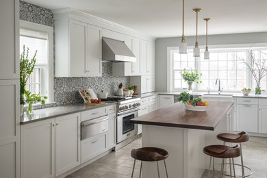 Design ideas for a transitional l-shaped kitchen in Boston with a farmhouse sink, shaker cabinets, white cabinets, wood benchtops, blue splashback, porcelain splashback, stainless steel appliances, with island and grey floor.