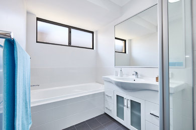 Modern kids bathroom in Perth with glass-front cabinets, white cabinets, a drop-in tub, white tile, ceramic tile, grey walls, ceramic floors, grey floor and a hinged shower door.