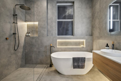 Inspiration for a mid-sized modern master bathroom in Sydney with medium wood cabinets, a freestanding tub, an open shower, gray tile, porcelain tile, grey walls, porcelain floors, engineered quartz benchtops, grey floor, an open shower, white benchtops, a single vanity and a floating vanity.