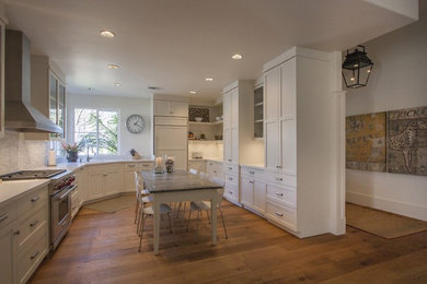This is an example of a large country u-shaped eat-in kitchen in San Francisco with an undermount sink, shaker cabinets, white cabinets, solid surface benchtops, white splashback, matchstick tile splashback, panelled appliances, light hardwood floors, with island and beige floor.