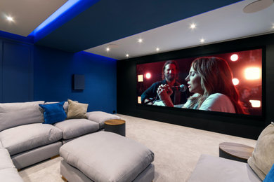 Expansive modern home cinema in Sussex with blue walls, carpet, a projector screen, grey floors and feature lighting.