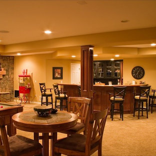 Imagen de sótano con puerta clásico, grande, con paredes amarillas, moqueta, chimenea de esquina y marco de chimenea de piedra