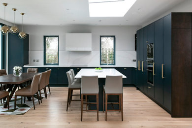 Design ideas for a large contemporary l-shaped eat-in kitchen in Dublin with an undermount sink, flat-panel cabinets, dark wood cabinets, quartzite benchtops, white splashback, black appliances, light hardwood floors, with island, white benchtop and beige floor.