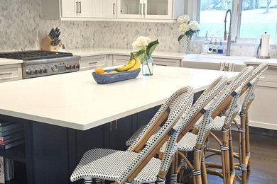 Example of a mid-sized minimalist u-shaped dark wood floor and brown floor eat-in kitchen design in New York with a farmhouse sink, shaker cabinets, white cabinets, quartz countertops, multicolored backsplash, marble backsplash, paneled appliances, an island and white countertops