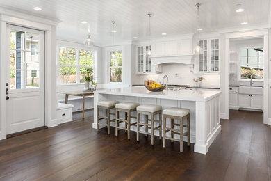 This is an example of a traditional kitchen in Other with a farmhouse sink, white cabinets, quartz benchtops, white splashback, porcelain splashback, medium hardwood floors and white benchtop.