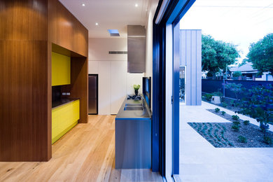 This is an example of a mid-sized contemporary l-shaped kitchen pantry in Adelaide with an integrated sink, flat-panel cabinets, medium wood cabinets, stainless steel benchtops, yellow splashback, glass tile splashback, stainless steel appliances, medium hardwood floors and no island.