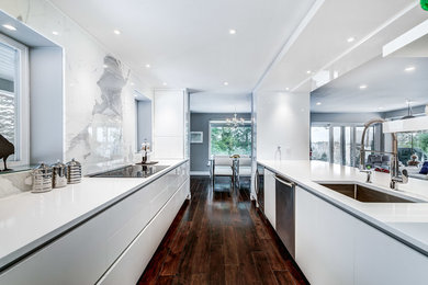 Example of a mid-sized minimalist galley dark wood floor and brown floor open concept kitchen design in Montreal with an undermount sink, flat-panel cabinets, white cabinets, solid surface countertops, white backsplash, stone slab backsplash, stainless steel appliances and no island
