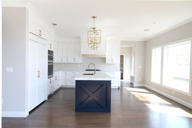 Inspiration for a transitional medium tone wood floor kitchen remodel in New York with an undermount sink, white cabinets, quartz countertops, white backsplash, porcelain backsplash, paneled appliances, an island and white countertops