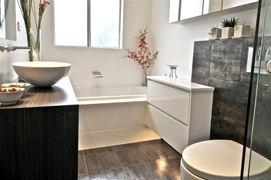 Inspiration for a modern master bathroom in Sydney with a vessel sink, flat-panel cabinets, solid surface benchtops, a drop-in tub, a corner shower, a wall-mount toilet, white tile, ceramic tile, white walls and porcelain floors.