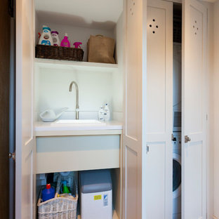 Design ideas for a small country single-wall laundry cupboard in Kent with a built-in sink, shaker cabinets, grey cabinets, quartz worktops, white walls, limestone flooring and a stacked washer and dryer.