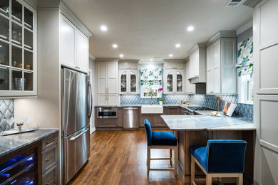 Enclosed kitchen - mid-sized transitional u-shaped medium tone wood floor and brown floor enclosed kitchen idea in Dallas with a farmhouse sink, recessed-panel cabinets, white cabinets, quartzite countertops, blue backsplash, porcelain backsplash, stainless steel appliances, a peninsula and multicolored countertops