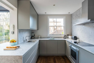 This is an example of a mid-sized contemporary u-shaped eat-in kitchen in London with an integrated sink, flat-panel cabinets, grey cabinets, marble benchtops, white splashback, marble splashback, stainless steel appliances, light hardwood floors, a peninsula and brown floor.