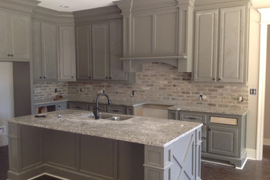 Example of an arts and crafts l-shaped dark wood floor eat-in kitchen design in Other with raised-panel cabinets, granite countertops, stainless steel appliances, an island, a double-bowl sink, gray cabinets, gray backsplash and brick backsplash