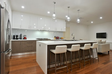 Large contemporary galley eat-in kitchen in Melbourne with a double-bowl sink, quartz benchtops, white splashback, glass sheet splashback, stainless steel appliances, medium hardwood floors and with island.
