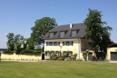 Großes Landhausstil Einfamilienhaus mit Putzfassade, gelber Fassadenfarbe, Walmdach und Ziegeldach in München