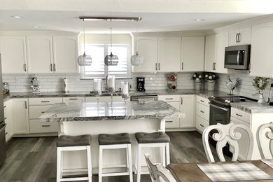 Foto på ett stort vintage grå kök, med en undermonterad diskho, skåp i shakerstil, vita skåp, granitbänkskiva, vitt stänkskydd, stänkskydd i tunnelbanekakel, rostfria vitvaror, laminatgolv, en köksö och grått golv