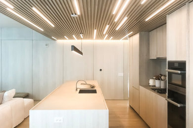 Inspiration for a mid-sized contemporary galley light wood floor and beige floor open concept kitchen remodel in Miami with an undermount sink, flat-panel cabinets, beige cabinets, paneled appliances, an island and beige countertops