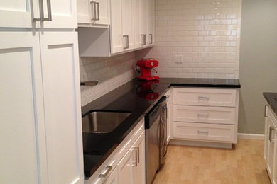 Inspiration for a small transitional galley light wood floor enclosed kitchen remodel in Los Angeles with an undermount sink, recessed-panel cabinets, white cabinets, solid surface countertops, white backsplash, subway tile backsplash, stainless steel appliances and no island