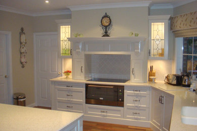 This is an example of a mid-sized traditional l-shaped eat-in kitchen in Newcastle - Maitland with recessed-panel cabinets, white cabinets, quartz benchtops, white splashback, with island and white benchtop.