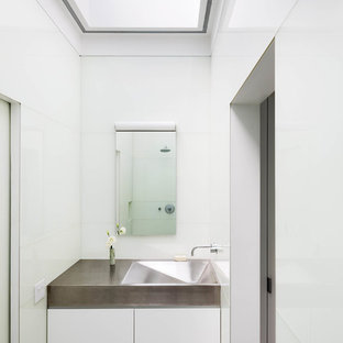 Idée de décoration pour une salle de bain minimaliste avec un lavabo intégré, un placard à porte plane, des portes de placard blanches, un plan de toilette en acier inoxydable, un mur blanc et un sol en marbre.