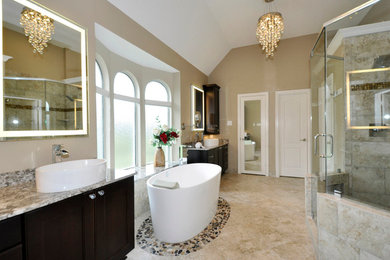 This is an example of a large transitional master bathroom in Houston with a vessel sink, recessed-panel cabinets, dark wood cabinets, a freestanding tub, an alcove shower, a one-piece toilet, beige walls, beige tile, travertine floors and granite benchtops.