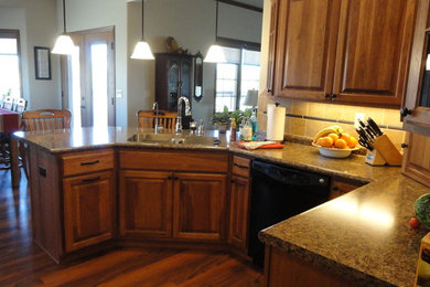 Inspiration for a mid-sized timeless l-shaped dark wood floor and brown floor eat-in kitchen remodel in Other with an undermount sink, raised-panel cabinets, medium tone wood cabinets, laminate countertops, stainless steel appliances, a peninsula, brown backsplash and ceramic backsplash