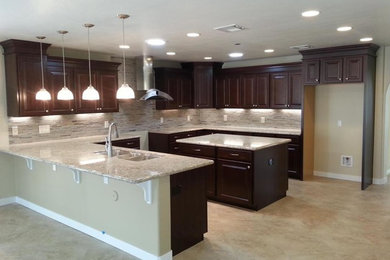 Inspiration for a large transitional u-shaped porcelain tile eat-in kitchen remodel in Phoenix with a double-bowl sink, raised-panel cabinets, dark wood cabinets, granite countertops, glass tile backsplash, an island, multicolored backsplash and stainless steel appliances