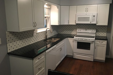 Small elegant l-shaped vinyl floor eat-in kitchen photo in Columbus with an undermount sink, flat-panel cabinets, white cabinets, granite countertops, white backsplash, ceramic backsplash and white appliances