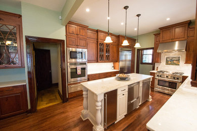 Example of a large classic u-shaped medium tone wood floor eat-in kitchen design in Little Rock with a farmhouse sink, raised-panel cabinets, dark wood cabinets, white backsplash, stone tile backsplash, stainless steel appliances and an island