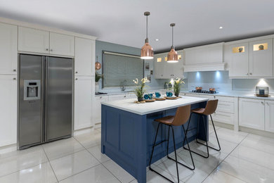 Inspiration for a transitional l-shaped kitchen in Dublin with recessed-panel cabinets, blue cabinets, blue splashback, stainless steel appliances, with island, white floor and white benchtop.