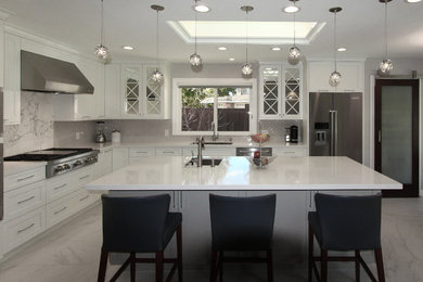 Photo of a mid-sized transitional l-shaped open plan kitchen in San Francisco with a single-bowl sink, recessed-panel cabinets, white cabinets, quartz benchtops, beige splashback, porcelain splashback, stainless steel appliances, with island, white floor and porcelain floors.