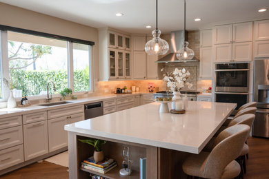 Example of a large transitional l-shaped vinyl floor and brown floor open concept kitchen design in San Diego with an undermount sink, shaker cabinets, white cabinets, quartz countertops, beige backsplash, porcelain backsplash, stainless steel appliances, an island and white countertops