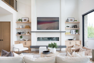 Modelo de sala de estar abierta contemporánea grande con paredes blancas, suelo de madera en tonos medios, todas las chimeneas, marco de chimenea de yeso, televisor colgado en la pared y suelo marrón
