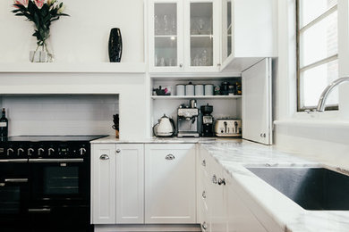 Inspiration for a mid-sized transitional l-shaped separate kitchen in Perth with an undermount sink, shaker cabinets, white cabinets, marble benchtops, subway tile splashback, black appliances, dark hardwood floors, with island and white splashback.