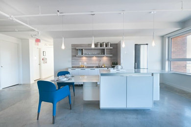 Example of a minimalist single-wall concrete floor eat-in kitchen design in Vancouver with an integrated sink, flat-panel cabinets, white cabinets, stainless steel countertops, gray backsplash, stainless steel appliances and an island