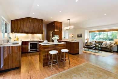 Open concept kitchen - mid-sized contemporary l-shaped medium tone wood floor and beige floor open concept kitchen idea in Houston with flat-panel cabinets, medium tone wood cabinets, beige backsplash, stone slab backsplash, stainless steel appliances, an island, an undermount sink and granite countertops