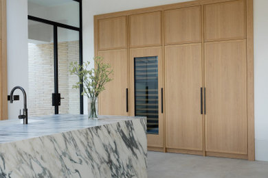 This is an example of an expansive contemporary open plan kitchen in London with flat-panel cabinets, light wood cabinets, marble worktops, marble splashback and an island.