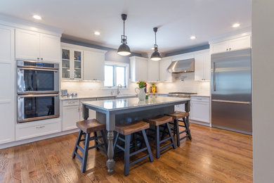 Open concept kitchen - large traditional l-shaped medium tone wood floor open concept kitchen idea in Boston with a farmhouse sink, shaker cabinets, white cabinets, quartzite countertops, white backsplash, subway tile backsplash, stainless steel appliances and an island