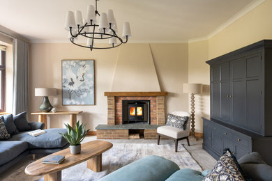 Design ideas for a medium sized rural living room in Hampshire with beige walls, carpet, a wood burning stove, a brick fireplace surround, a concealed tv, beige floors and a chimney breast.