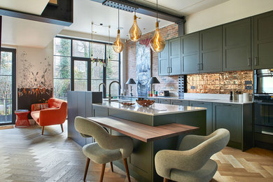 Inspiration for an expansive contemporary l-shaped open plan kitchen in London with a double-bowl sink, flat-panel cabinets, green cabinets, quartz worktops, glass tiled splashback, black appliances, light hardwood flooring, an island, beige floors, grey worktops, exposed beams and a feature wall.