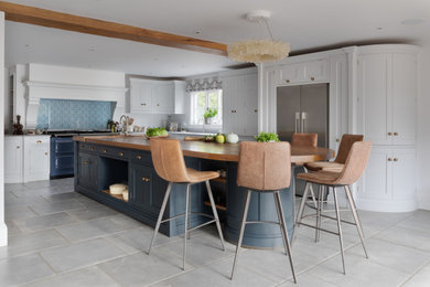 This is an example of a large traditional l-shaped eat-in kitchen in Surrey with a drop-in sink, shaker cabinets, white cabinets, wood benchtops, blue splashback, glass sheet splashback, stainless steel appliances, porcelain floors, with island, grey floor, brown benchtop and exposed beam.