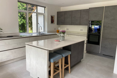 Design ideas for a medium sized contemporary l-shaped kitchen/diner in Buckinghamshire with a built-in sink, flat-panel cabinets, grey cabinets, quartz worktops, black appliances, porcelain flooring, an island, grey floors, white worktops and feature lighting.