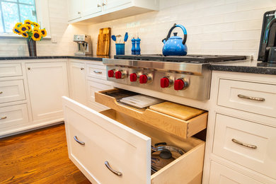 Example of a large transitional l-shaped medium tone wood floor and brown floor kitchen design in New York with an undermount sink, beaded inset cabinets, white cabinets, soapstone countertops, white backsplash, subway tile backsplash, paneled appliances, an island and black countertops