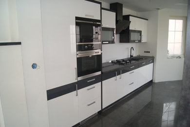 Foto på ett mellanstort funkis linjärt kök med öppen planlösning, med en nedsänkt diskho, vita skåp, träbänkskiva, vitt stänkskydd, rostfria vitvaror och klinkergolv i keramik