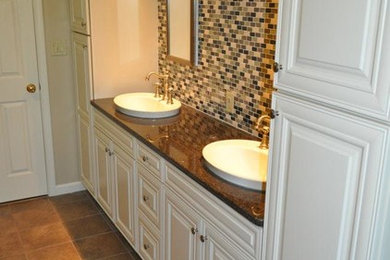 Large trendy master beige tile and ceramic tile ceramic tile and brown floor bathroom photo in Other with raised-panel cabinets, white cabinets, beige walls, a drop-in sink, granite countertops and a hinged shower door