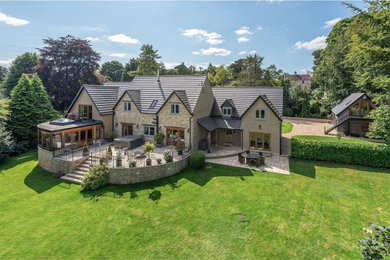 This is an example of a large and beige rustic two floor rear house exterior in Gloucestershire with a pitched roof, a tiled roof and a grey roof.