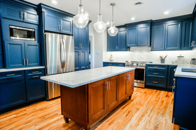 ウィルミントンにあるラグジュアリーなトランジショナルスタイルのおしゃれなキッチン (落し込みパネル扉のキャビネット、青いキャビネット、クオーツストーンカウンター、白いキッチンパネル、クオーツストーンのキッチンパネル、無垢フローリング、茶色い床、白いキッチンカウンター) の写真
