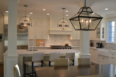 Mid-sized transitional l-shaped dark wood floor eat-in kitchen photo in New York with a farmhouse sink, shaker cabinets, white cabinets, marble countertops, gray backsplash, stone tile backsplash, stainless steel appliances and an island