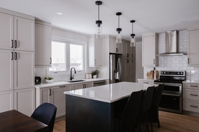 Mid-sized transitional l-shaped light wood floor and brown floor eat-in kitchen photo in Other with an undermount sink, shaker cabinets, beige cabinets, quartz countertops, white backsplash, subway tile backsplash, stainless steel appliances, an island and white countertops